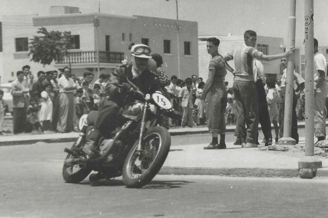 A rider on a motorcycle races around a corner while the audience watches the race.