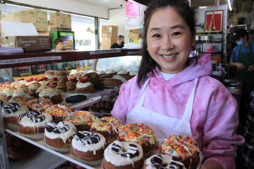 Woman in pick sweatshirt holding tray of donuts 